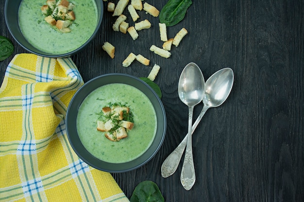 Creamy spinach soup with crackers, herbs and chia seeds. Green soup served in a bowl on a wooden table. . Flat lay.