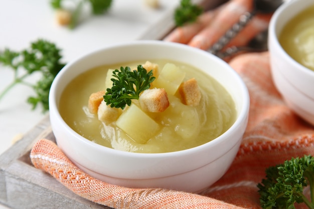 Creamy sweet potato soup with croutons and parsley in white bowl