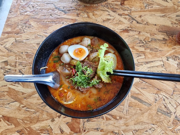 Creamy Tom Yum Noodles In a black bowl served with squid prawns meatballs lettuce and boiled egg Closeup shot focusing on selected point