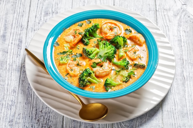 Creamy Tomato Soup with Shrimp and Broccoli in a blue bowl on a white wooden table, american cuisine