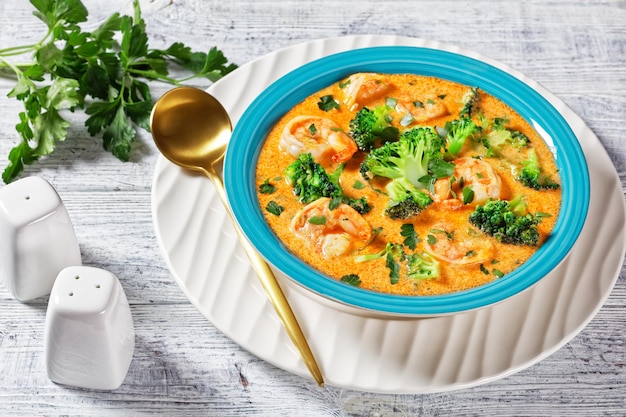 Creamy Tomato Soup with Shrimp and Broccoli in a blue bowl on a white wooden table, american cuisine