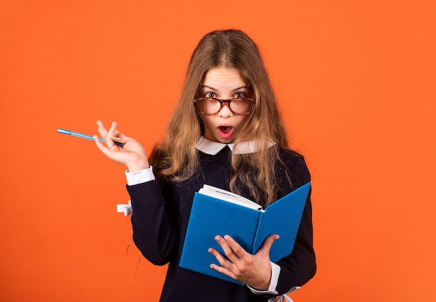 Create and surprise. Surprised schoolgirl with pen and book brown background. Little child keep mouth opened of surprise. Smart look. Nerdy girl. School and education. Surprise concept. Surprise idea.