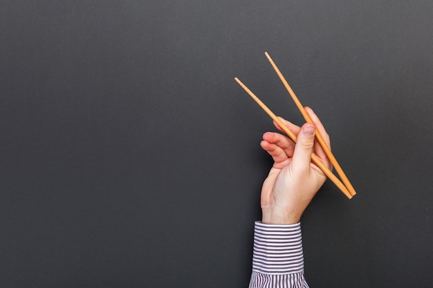 Creatief beeld van houten eetstokjes in mannelijke handen op zwarte achtergrond. japans en chinees eten met copyspace