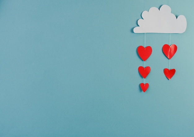 Creatief concept vakantie Valentijnsdag liefde foto van handgeschept papier wolk regent met harten op blauwe achtergrond.