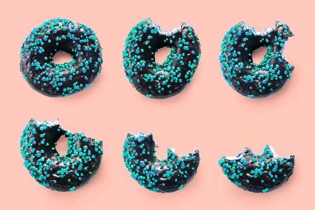 Creatief concept van bijten eten van heerlijke zoete suiker zwarte donut donut met blauwe glazuur op roze achtergrond. Bovenaanzicht plat lag ongezond dessert Voedselconcept.