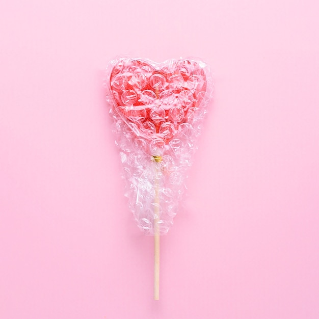 Creatief concept voor geestelijke gezondheid. Enkele hartvormige lolly verpakt in bubblegum op een roze achtergrond.