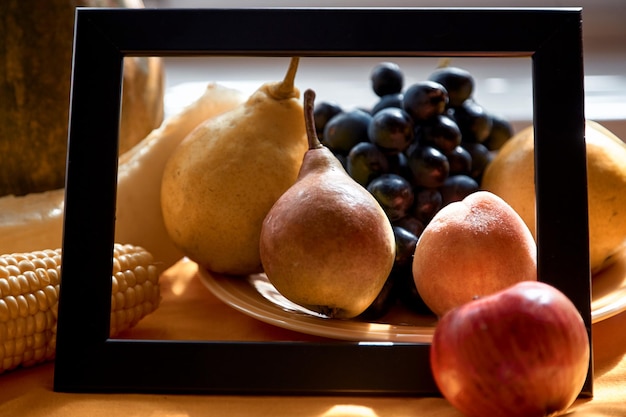 Creatief fruitframe van druiven, appel, peer, perzik, maïs en meloen op de oranje plaat onder zonlicht