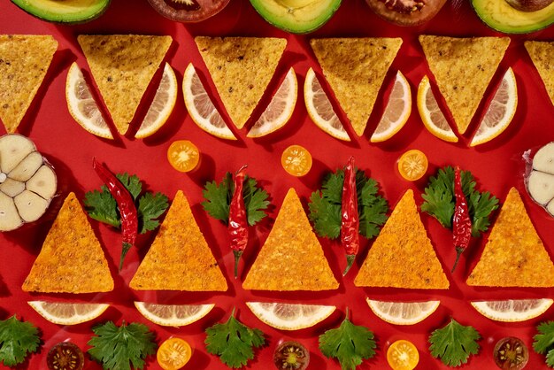 Creatief geometrisch voedselpatroon van mexicaanse nacho's maïsspaanders, verse groenten, fruit, greens, spaanse peper, knoflook - ingrediënten voor chilisaus van de tomaat op een rode achtergrond. plat leggen