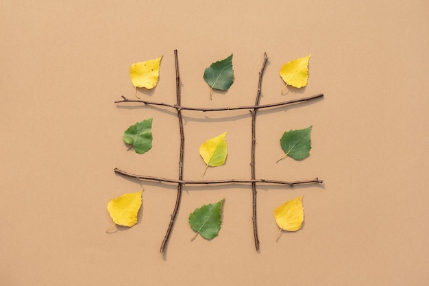 Creatief herfstconcept groene en gele bladeren in raster gemaakt van takken op bruine achtergrond bovenaanzicht plat leggen