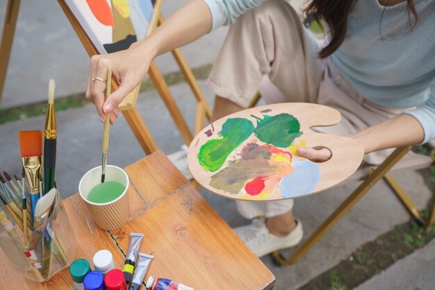 Creatief kunstconcept Vrouwelijke artiest wast penseel tijdens het schilderen van kunst op canvas in de tuin