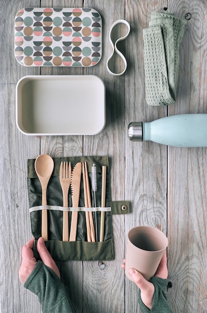 Creatief plat lag, afvalconcept zonder afval met set van herbruikbaar houten bestek, lunchbox, drinkfles en herbruikbare koffiekop. Bovenaanzicht van duurzame levensstijl, vlakke indeling op verouderd hout.