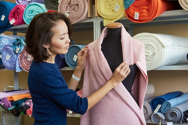 Creatieve aziatische modeontwerper vouwt roze stof op een mannequin in haar atelier