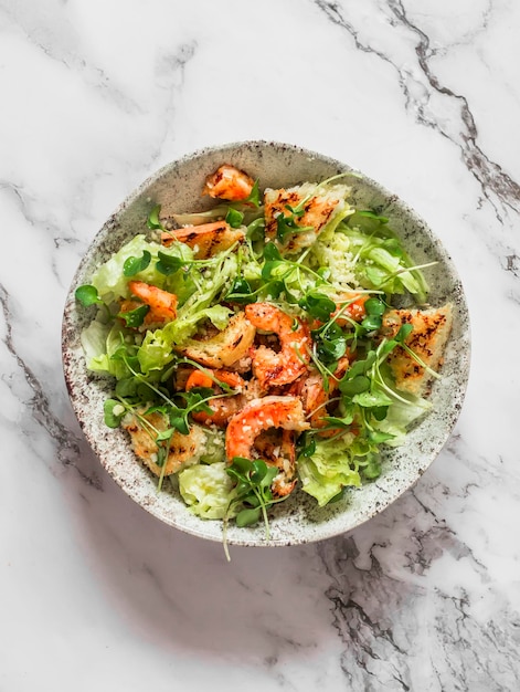 Creatieve Caesar-salade met gegrilde garnalen op een lichtmarmeren bovenaanzicht als achtergrond