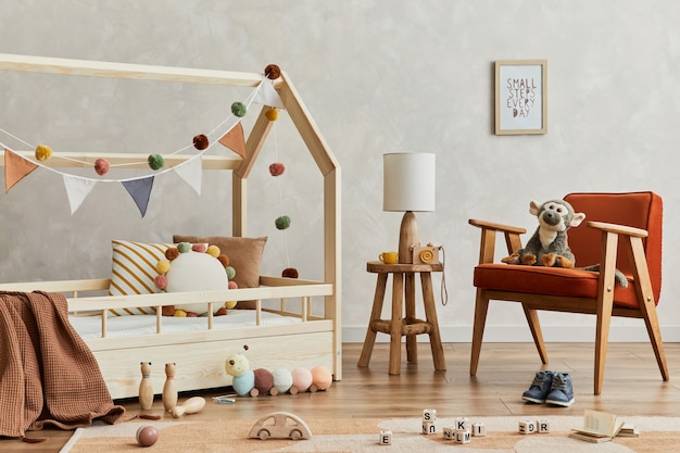 Creatieve compositie van gezellig Scandinavisch kinderkamerinterieur met houten bed, rode fauteuil, pluche en houten speelgoed en hangende textieldecoraties. Creatieve muur, tapijt op de vloer. Sjabloon.