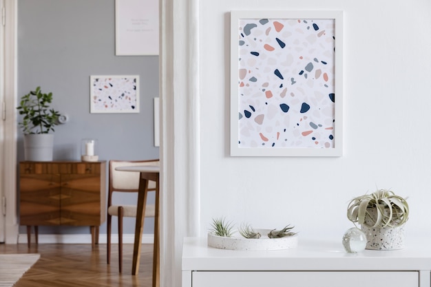 Creatieve compositie van stijlvol scandi woonkamer interieur met mock-up posterframes, houten commode, stoel, planten en accessoires. Neutrale wanden, parketvloer. Sjabloon.