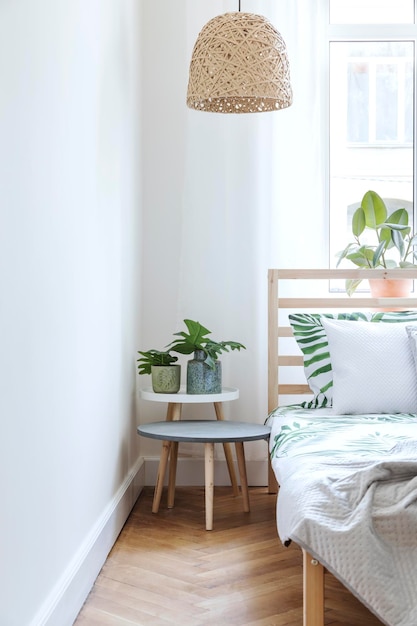 Creatieve compositie van stijlvolle scandinavische slaapkamer met houten bed salontafel planten kussens en textielaccessoires Witte muren en parketvloer