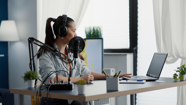 Creatieve contentmaker in studio die zich klaarmaakt voor internet live podcast. Radiopresentator bespreekt laatste nieuws met publiek terwijl hij professionele audioapparatuur op zijn bureau heeft.