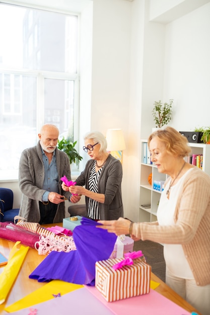 creatieve grijsharige mensen die aan tafel staan terwijl ze samen cadeaus inpakken