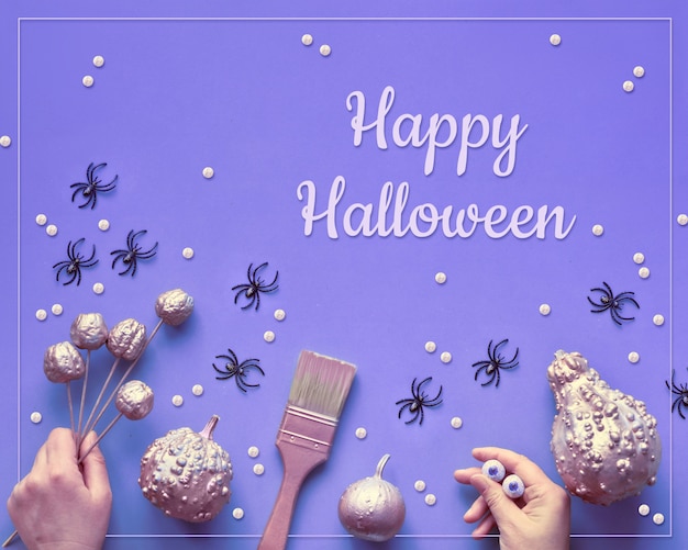 Creatieve Halloween neon plat lag op paars papier, tekst "Happy Halloween". Pompoenen geverfd metallic roze, handen, kwast, handmonster met chocoladeogen.