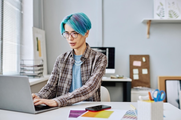 Creatieve jonge man met blauw haar met behulp van laptop op kantoor