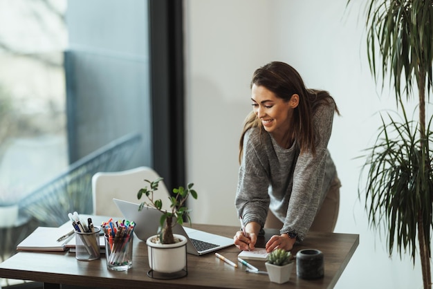 Creatieve jonge vrouw die aan een laptop werkt in haar thuisstudio
