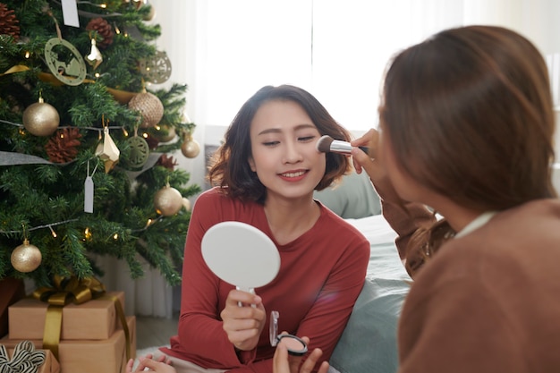 Creatieve jonge vrouw die make-up aanbrengt op het gezicht van een vriend in de woonkamer