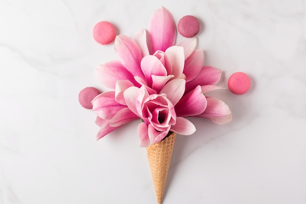 Creatieve lay-out gemaakt met roze magnolia bloemen in wafelkegel met bitterkoekjes. Plat leggen