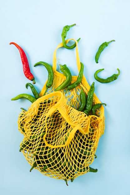 Foto creatieve lay-out groene chili pepers. groene groenten in gele stringzak. hoop groene peper genaamd frigitelli