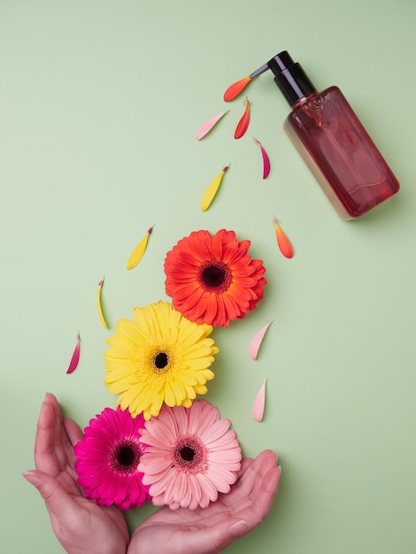 Creatieve lente conceptontwerp Handen plukken van kleurrijke bloemen en besprenkelde bloemblaadjes die uit een amberkleurige dispenserfles komen Platte plaatsing op groene achtergrond