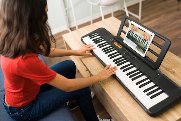 Creatieve meid met artistieke vaardigheden die online muzieklessen neemt met een mannelijke leraar tijdens een videogesprek en thuis piano speelt