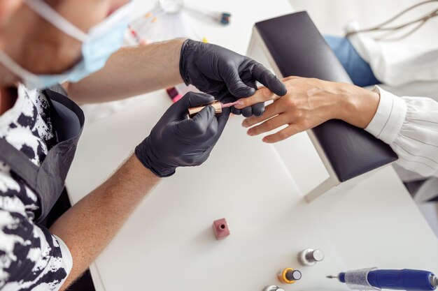 Creatieve nagelmeester die nagels van zijn cliënt in salon verwerkt