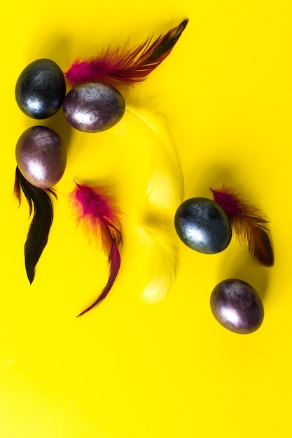 Creatieve Pasen-compositie. paarse eieren en veren op een gele achtergrond. bovenaanzicht. plat liggen.