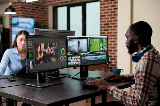 Creatieve professionele videograaf op kantoor zittend op een werkstation met meerdere monitoren tijdens het bewerken van digitale beelden. Visuele editor van de postproductieafdeling die de videokwaliteit verbetert.