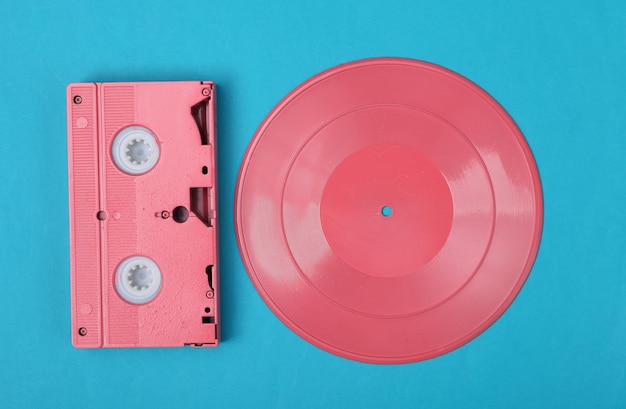 Creatieve retro 80s lay-out Roze vinylplaat en vhs op blauwe achtergrond Minimalisme Plat lag Bovenaanzicht