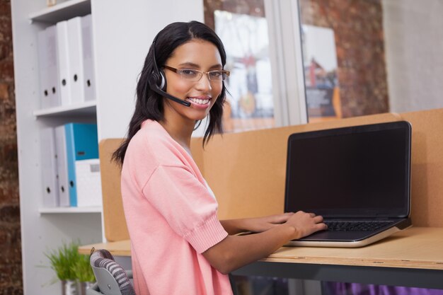 Creatieve vrouw met hoofdtelefoon die computer met behulp van bij bureau