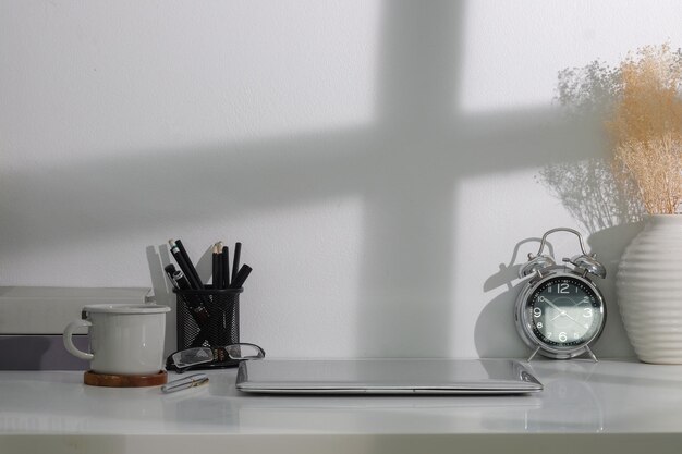 Creatieve werkplek met computer laptop koffiekopje wekker en boeken op witte tafel