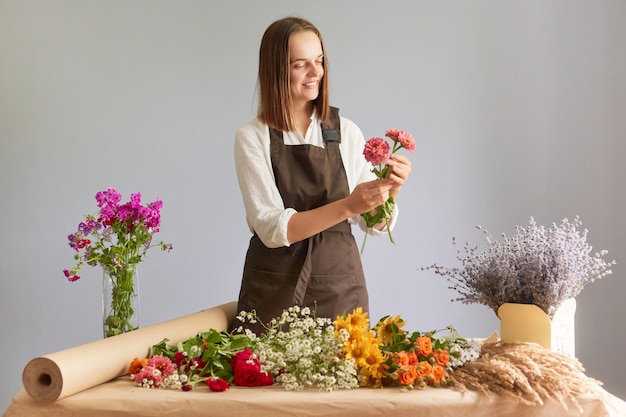 Creatieve werkruimte decor Markt voor biologische bloemen Aantrekkelijke gelukkige vrouw bloemist creëren mooi boeket op werkplek in bloemenwinkel staande geïsoleerd over grijze achtergrond