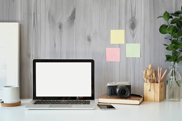 Creatieve werkruimte, leeg scherm laptop, model poster en vintage camera op bureau