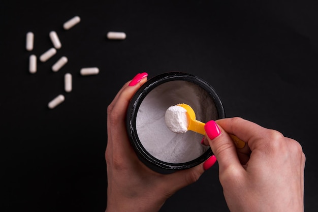 Creatine De hand van een vrouw houdt een portie sportvoeding vast op een zwarte achtergrond close-up