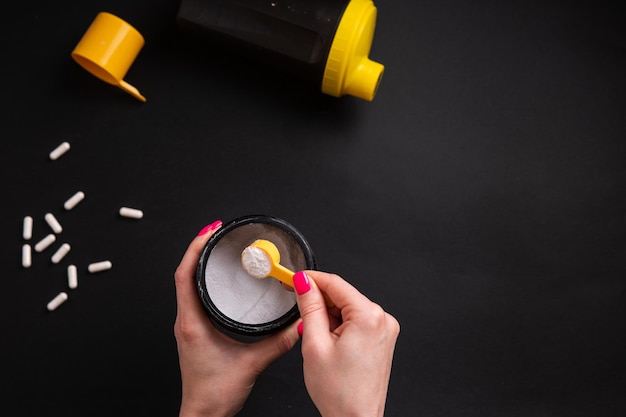 Creatine A woman's hand holds a portion of sports nutrition on a black background closeup