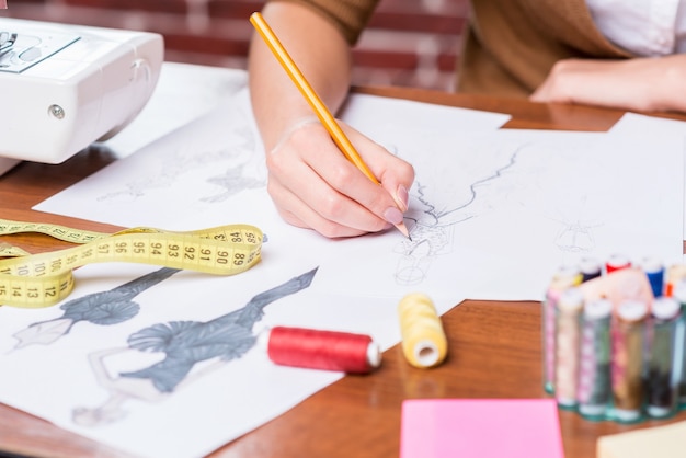 Creating new fashion look. Close-up of woman drawing fashion sketch while sitting at her working place