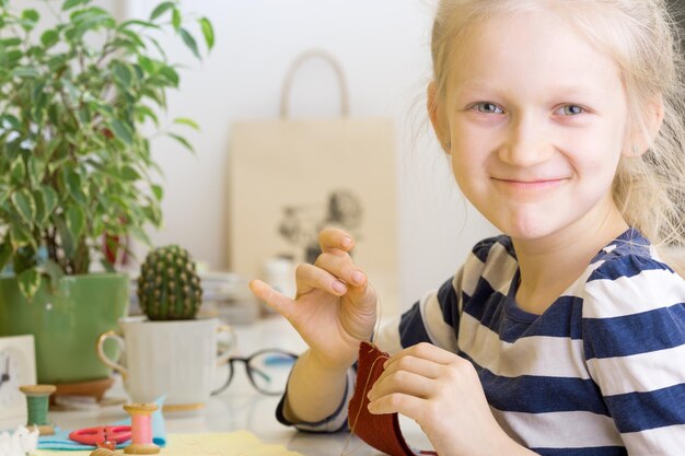 創造。小さな女の子はフェルトで作られたおもちゃを縫う