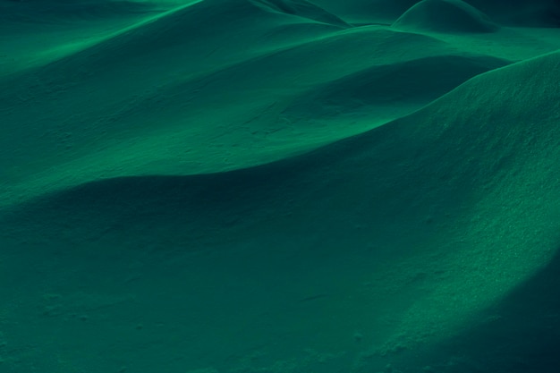 Creative abstract winter background toned in deep green color. Play of light and shadow on undulating slopes of snowdrifts.