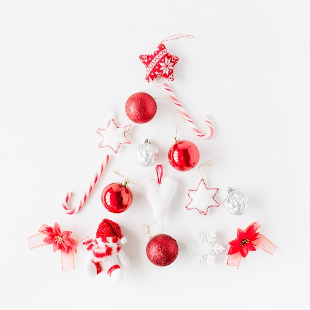 Disposizione creativa dell'albero di natale rosso brillante fatto di palla di natale, dolci, giocattoli su bianco