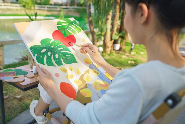 写真 創造的なアートのコンセプト 公園に座って幸せな気持ちでキャンバスに絵を描く女性アーティスト