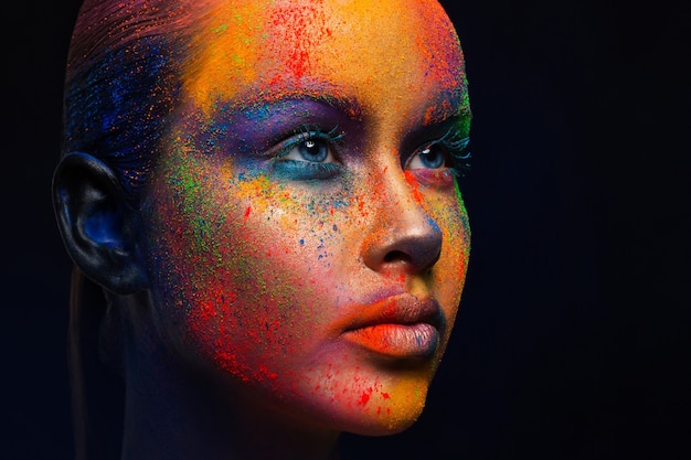 Creative art make up. Holi colors. portrait of young fashion model with bright colorful mix of paint on her face.