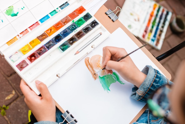 Creative artist paints a colorful picture. Close-up of hands and brush in the process of painting outdoors