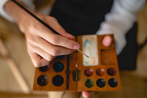 Artista creativo che lavora sull'arte dei colori per disegnare foto con vernice a pennello in hobby, laboratorio artigianale di strumenti per pennelli ad acquerello con tela in studio, cavalletto per tavolozza e sfondo di design di opere d'arte