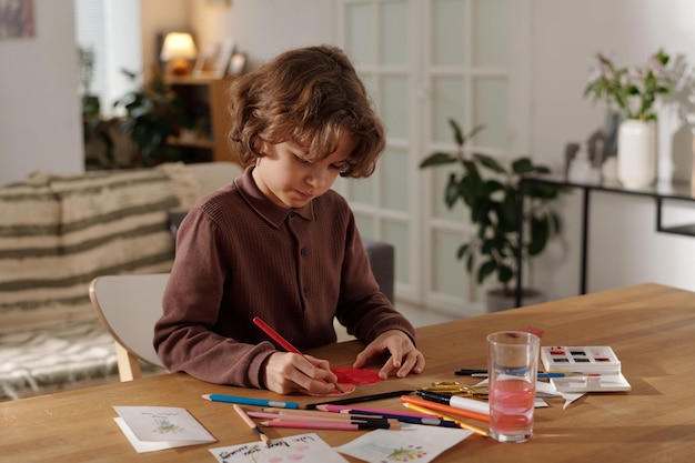 Creative boy drawing heart on postcard