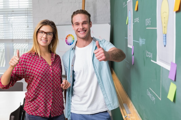 Creative business people gesturing thumbs up by blackboard